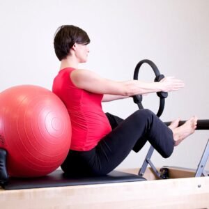 Pregnant woman in gym doing Pilates exercise with reformer and stability ball.